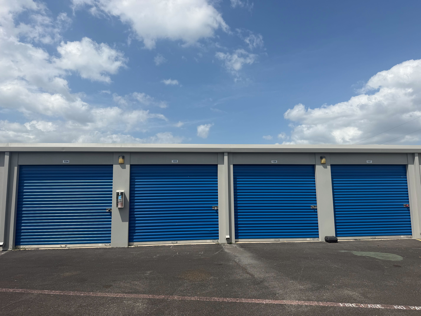 Row of blue roll-up storage unit doors numbered 104 through 107 along a paved drive aisle