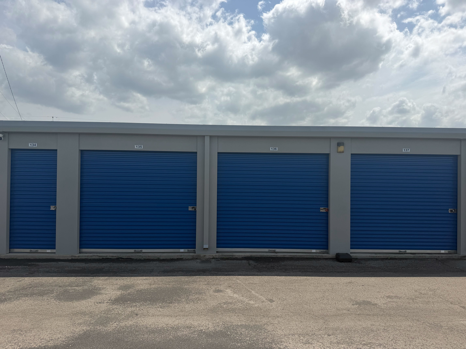 Row of blue roll-up unit doors numbered 134 through 137 along a paved drive aisle