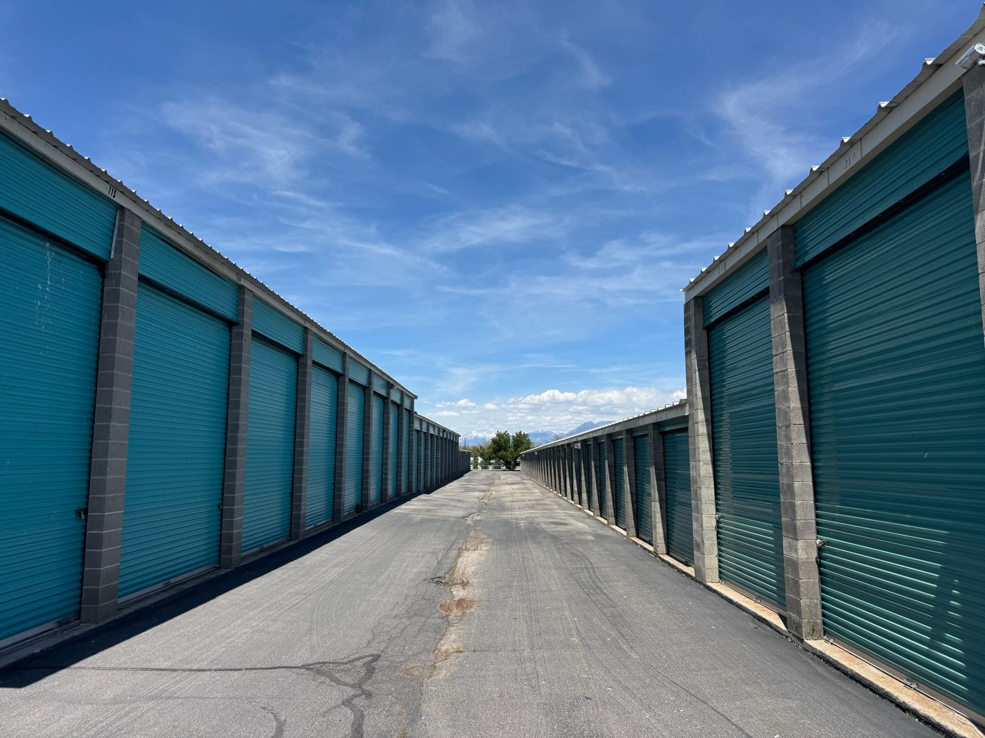 Rows of teal drive-up storage units with a wide paved aisle
